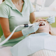 Zahnärztin in einem hellen Behandlungsraum, die mit Handschuhen und einem zahnärztlichen Instrument die Zähne einer liegenden Patientin behandelt