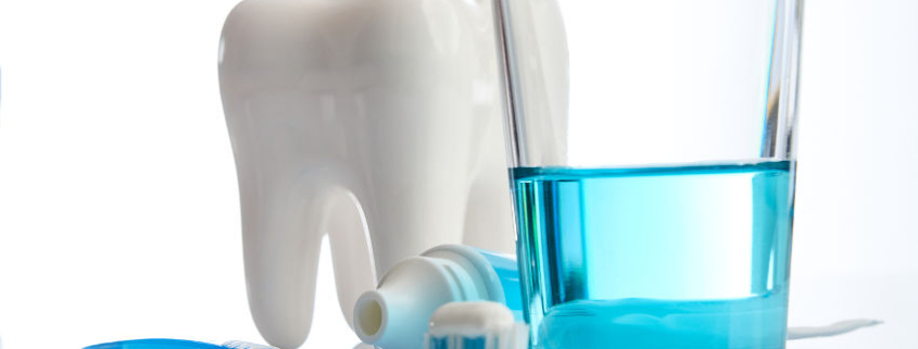 Sportler und Zahnpflege – gründliche Mundhygiene als wichtiger Schutz vor Zahnschäden und Zahnproblemen durch säurehaltige und zuckerhaltige Sportdrinks bei intensiver körperlicher Belastung. Das Bild zeigt exemplarisch ein Zahn sowie Putzutensilien wie Zahnbürste, Zahnpasta und ein Becher mit eine antiseptische blaue Mundspülung