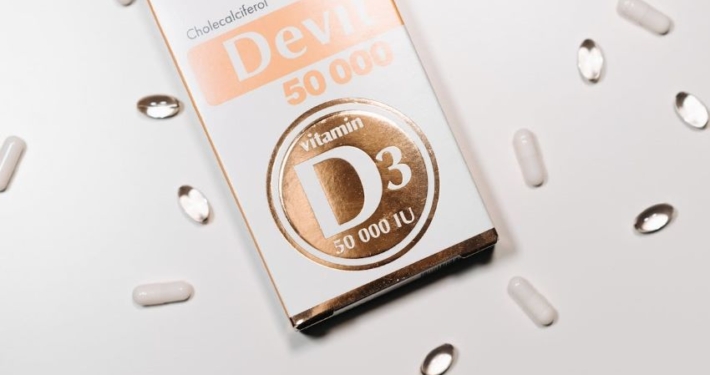 Verpackung von Vitamin D3 50.000 IU Cholecalciferol-Softgel-Kapseln, umgeben von weißen und durchsichtigen Kapseln auf weißem Hintergrund.