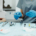 Ein Zahnarzt mit blauen Handschuhen hält ein Zahnspiegel, bereit für eine Untersuchung oder Behandlung, mit verschiedenen zahnärztlichen chirurgischen Instrumenten und Materialien auf einem Tablett im Vordergrund als Vorbereitung für eine Weisheitszahn-Entfernung. Der Patient ist außerhalb des Fokus, und der Hintergrund zeigt einen Teil des zahnmedizinischen Behandlungsstuhls und der Praxisumgebung